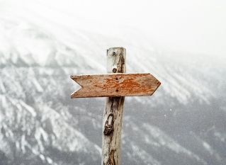 A wooden arrow signpost points the way amidst a snowy mountain landscape.